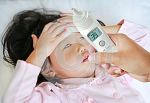 Closeup mother hand takes temperature for her daughter with high pressure of ear thermometer on bed at home