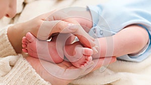 Closeup of mother holding little feet of her newborn baby lying on bed
