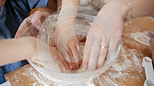 Closeup of mother's and child's hands kneading dough ingredients in glass bowl while making biscuits. Children cooking