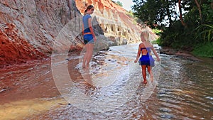 Closeup mother small daughter in blue gambol barefoot in shallow stream