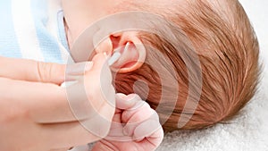 Closeup of mother using cotton swabs to clean little baby's ears from ear wax. Concept of babies and newborn hygiene and