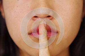 Closeup mouth of young brunette woman, finger covering lips as in silence, facing camera, hostage concept