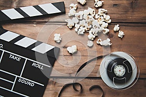 Closeup of movie camera with film reel clapper board and popcorn on wood.