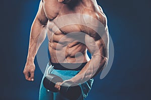 Closeup of a muscular young man lifting dumbbells weights on dar