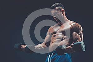 Closeup of a muscular young man lifting dumbbells weights on dar