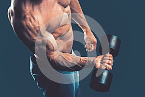 Closeup of a muscular young man lifting dumbbells weights on dar