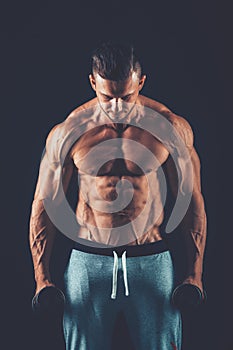 Closeup of a muscular young man lifting dumbbells weights on dar