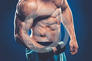 Closeup of a muscular young man lifting dumbbells weights on dar