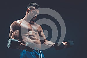 Closeup of a muscular young man lifting dumbbells weights on dar