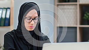 Closeup Muslim business woman in black headscarf working chatting surfing internet use laptop