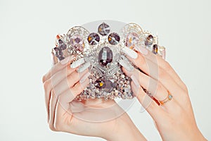 Closeup nail polished pastel multicolored long nails coral pink white with crystals hand holding black dark diamond crown broach