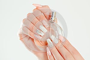 Closeup nail polished pastel multicolored long nails coral pink, white with crystals, hand holding perfume bottle isolated on