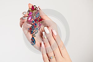 Closeup nail polished pastel multicolored long nails coral pink, white with crystals, hand holding perfume pink blue green broach