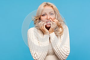 Closeup nervous anxious blond woman in white sweater biting her nails on fingers, panicking, waiting for test results, phobia