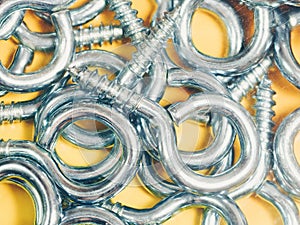 Closeup of new shiny metallic eyebolt screws on a yellow background