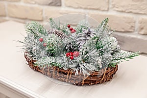 Closeup New Year wicker basket with snow covered spruce evergreen branches, cones red berries. Concept christmas decor, table