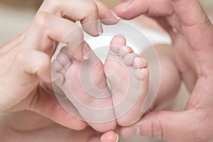 Closeup of newborn baby feet. Baby feet in mother hands. Family hearth shape. Love and care. Mom and dad love.