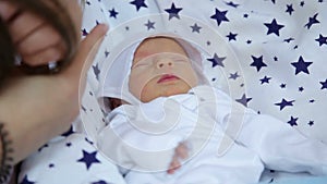 Closeup of newborn baby sleeping in a crib, mom gently stroking her newborn baby