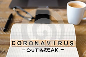 Closeup on notebook over wood table background, focus on wooden blocks with letters making Coronavirus Outbreak writing