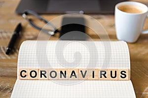 Closeup on notebook over wood table background, focus on wooden blocks with letters making Coronavirus writing