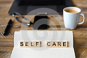 Closeup on notebook over wood table background, focus on wooden blocks with letters making Self Care writing