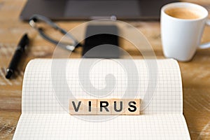 Closeup on notebook over wood table background, focus on wooden blocks with letters making Virus writing