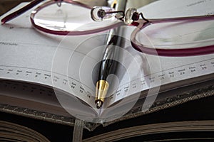 Closeup of notebook, pen and glasses.