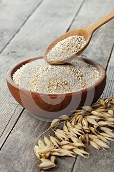 closeup of oat bran in bowl and in spoon with dry ears near on table