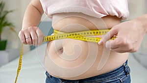 Closeup of obese woman measuring her big belly with yellow measuring tape. Concept of dieting, unhealthy lifestyle