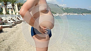 Closeup of a obese young man at the seaside, taking a moment to manage his belly before swimming on sea beach, as part