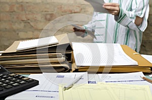 Closeup of office desk and lot of documents on it and woman analyzing business reports on the background