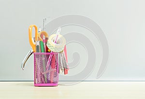 Closeup office equipment with pink steel box for pen on blurred wooden desk and frosted glass wall textured background in the work