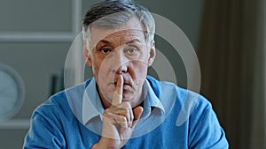 Closeup old caucasian 60s man holding index finger near mouth stop talking hush gesture silence sign elderly mature