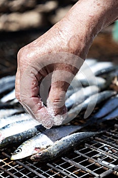 Old woman salting some sardines in a grill photo