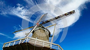 Closeup of old dutch windmill sails against blue sky with windblown clouds - wind energy conversion concept