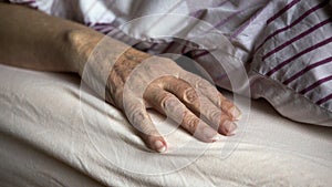 Closeup of old female hand in bed