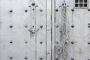 Closeup of old Iron door with closed padlock on a chain. A chain of silver color with closed padlock on an old gate.