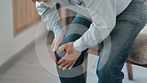 Closeup old man stroking knee feeling pain injury or chronic disease trying stand up to chair