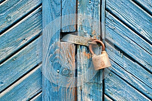 Closeup of old padlock on a weathered retro blue wooden door. Textured background.