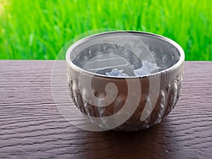 Closeup old Thai style silver cup with cold water inside on wooden table