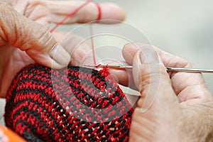 Closeup old woman in countryside, Thailand knitting by knitting needle and red and black yarn doing handmade bags at her home