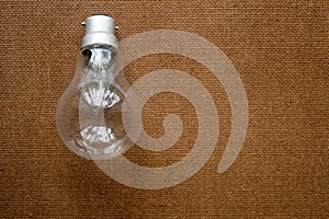 Closeup of Older style Incandescent Clear Light bulb placed over Brown Color Hard cork board. Creative background design ideas for