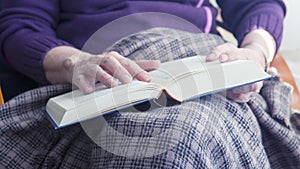 Closeup of older woman sitting by window and reading a book