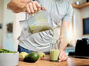 Closeup of one caucasian man pouring healthy green detox smoothie from blender into glass in kitchen at home. Guy having