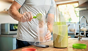 Closeup of one caucasian man pouring a scoop of chocolate whey protein powder to a health shake for energy for training