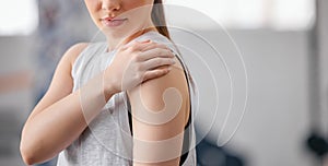 Closeup of one caucasian woman holding her sore shoulder while exercising in a gym. Female athlete suffering with