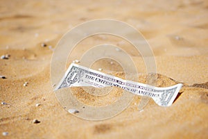 Closeup of one dollar banknote buried in the sand. Copy space