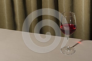 Closeup of one glass of red wine on the table against folds of curtains.Empty space.Hard light