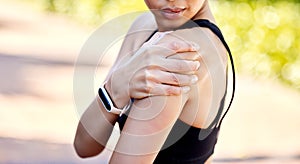 Closeup of one mixed race woman holding her sore shoulder while exercising outdoors. Female athlete suffering with