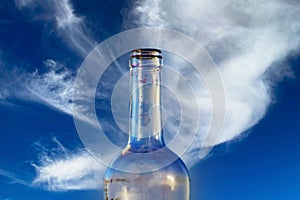 Closeup of one single isolated empty transparent red wine alcohol glass bottle, clear blue sky and fluffy white cloud background